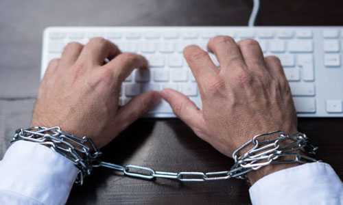 Businessman hands tied with chains on wrists typing on laptop keyboard